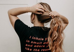 Woman with honey-blonde hair pulling her hair into a ponytail